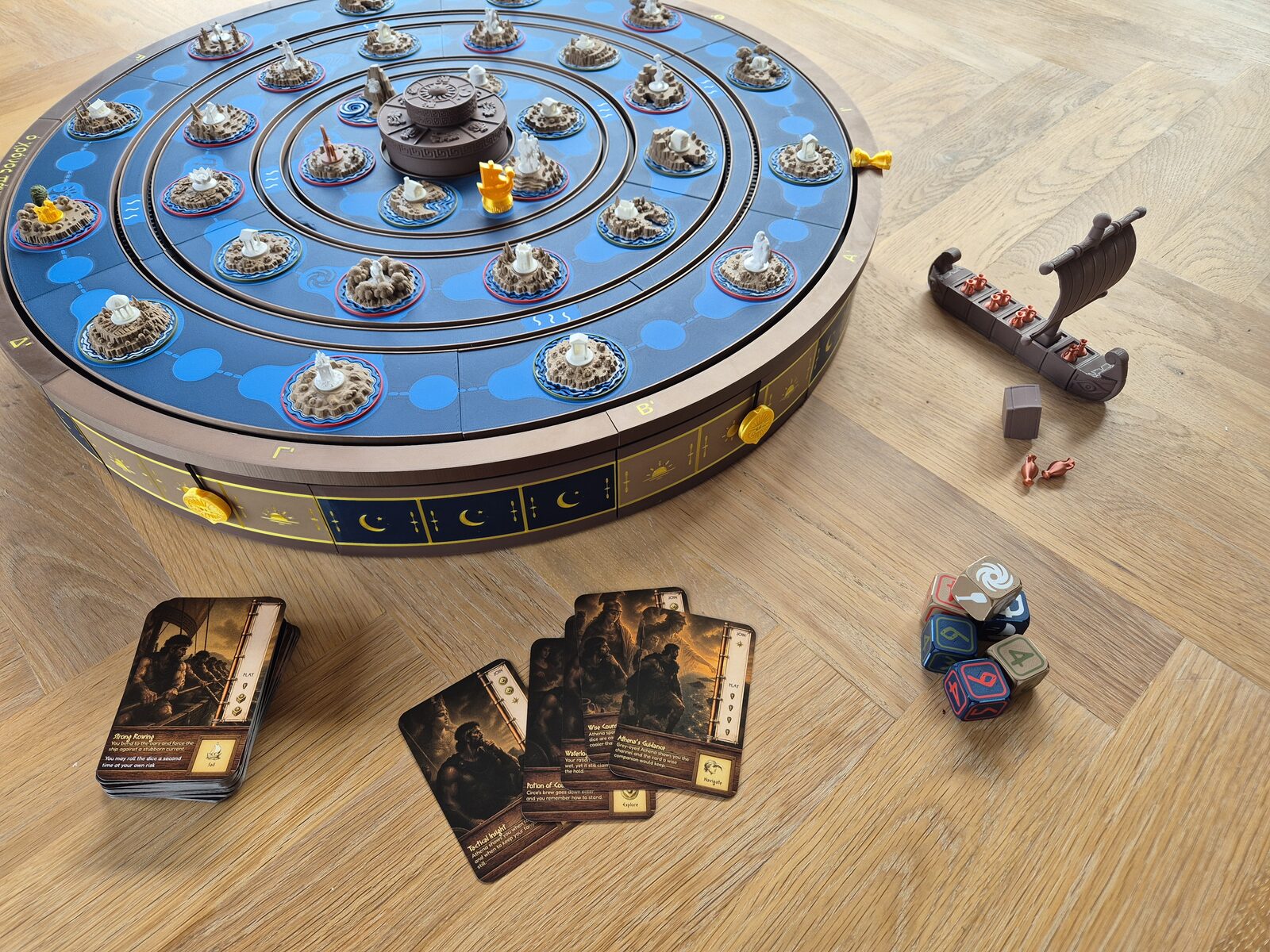 The full printed board with rotating sea rings, the ship, dice, and cards laid out beside it.